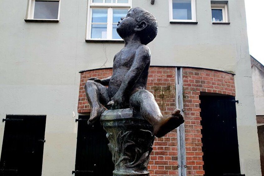 Une statue d’un enfant assis sur un piédestal devant un bâtiment doté de fenêtres et d’un mur en briques. 2