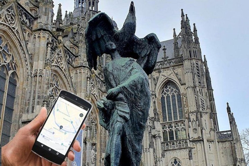 Une personne tenant un smartphone sur lequel est affichée une application de cartographie, se tenant devant une cathédrale de style gothique aux détails architecturaux complexes. 1