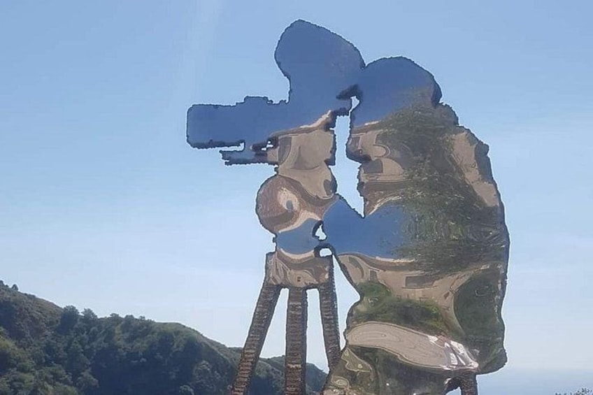 A large sculpture of two figures embracing, set against a backdrop of a clear sky and a hilly landscape. 2