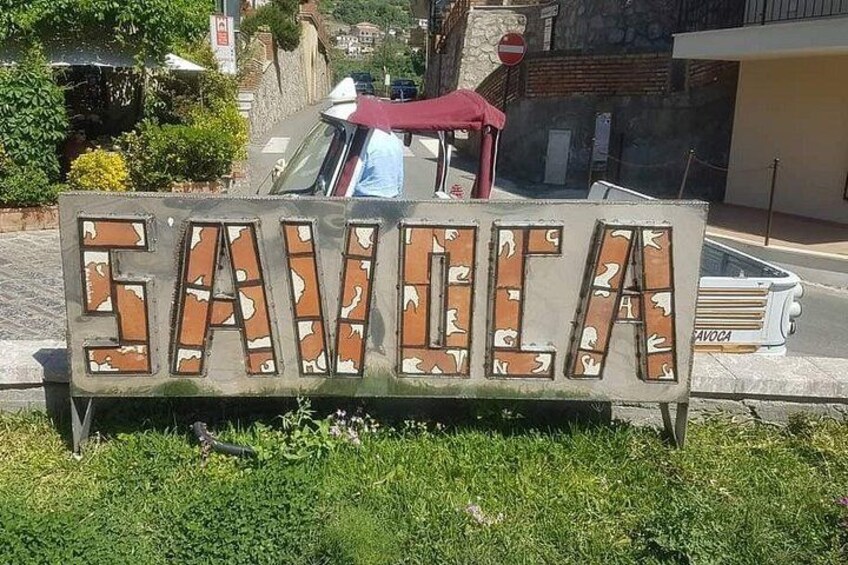 A sign with the word 'SAVOCA' in large letters, surrounded by greenery. 3