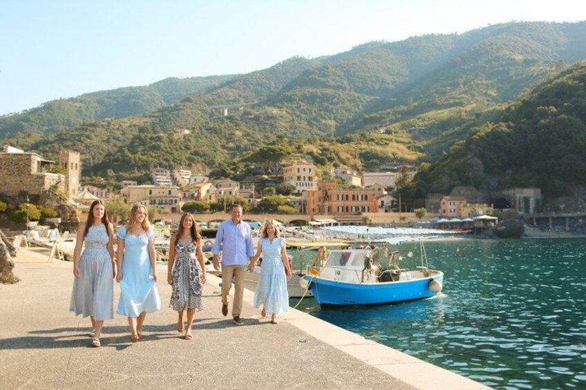 A group of people walking along a waterfront promenade with a boat docked nearby, set against a backdrop of hills and buildings. 5