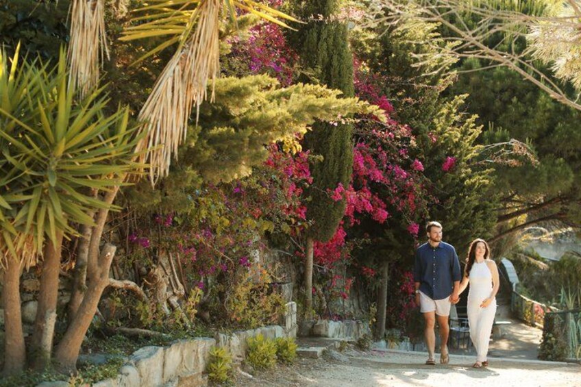 A couple walking on a path surrounded by lush greenery and flowering plants. 3