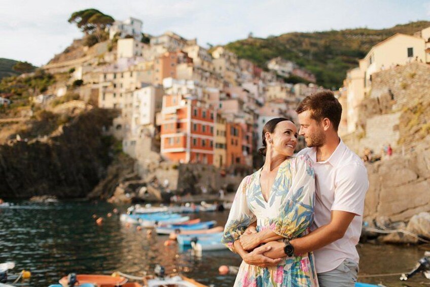 A couple embracing on a rocky seaside with colorful buildings in the background. 1