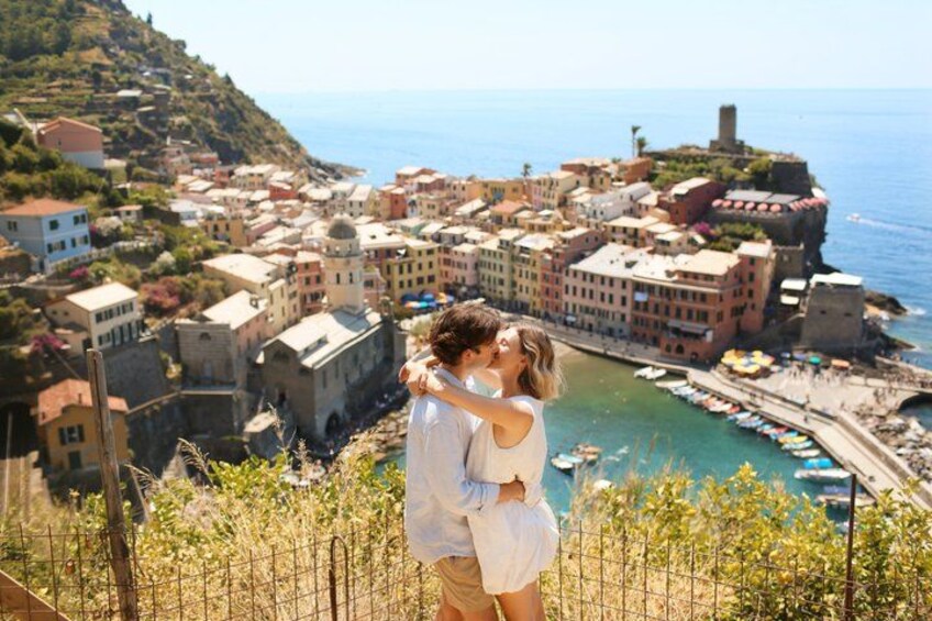 A couple embracing on a hill overlooking a coastal town with historic buildings and boats. 2