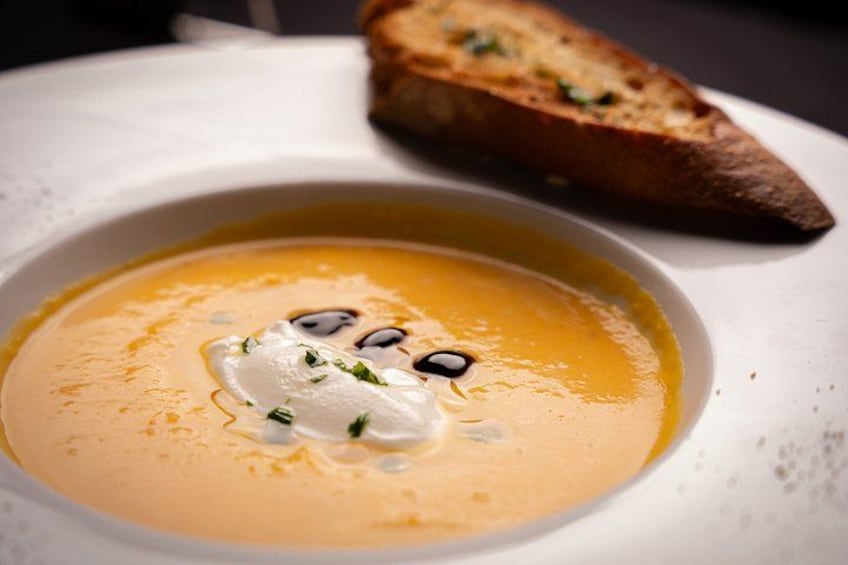 A bowl of soup with a dollop of cream and a piece of bread on the side. 3
