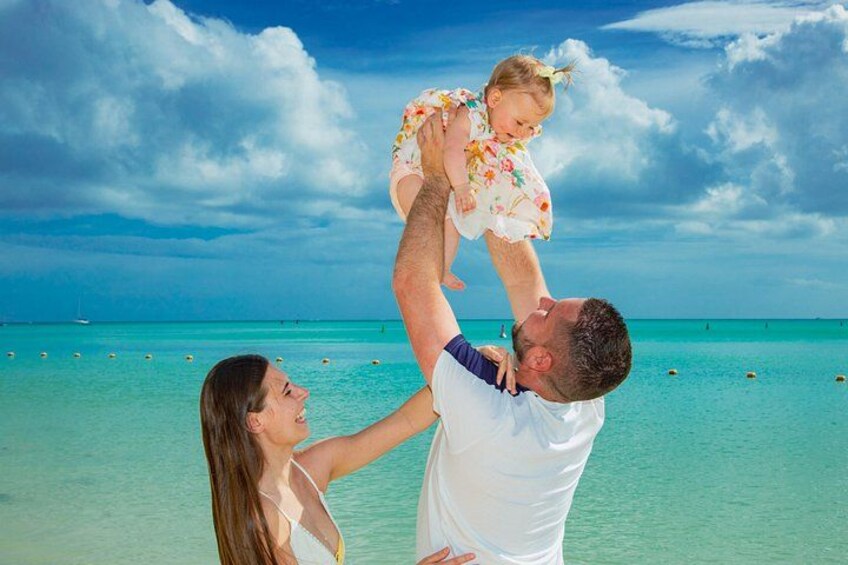 A man lifting a child on a beach with clear turquoise water and a partly cloudy sky. 3
