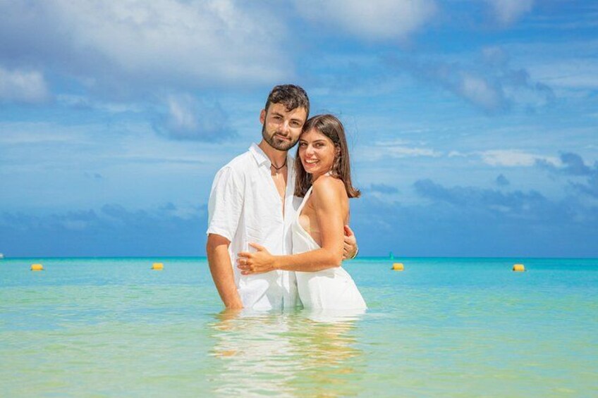 A couple embracing in shallow water with a clear blue sky and ocean in the background. 2