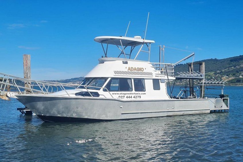 A white boat named 'ADAGIO' docked at a pier with a clear blue sky and calm water in the background. 4