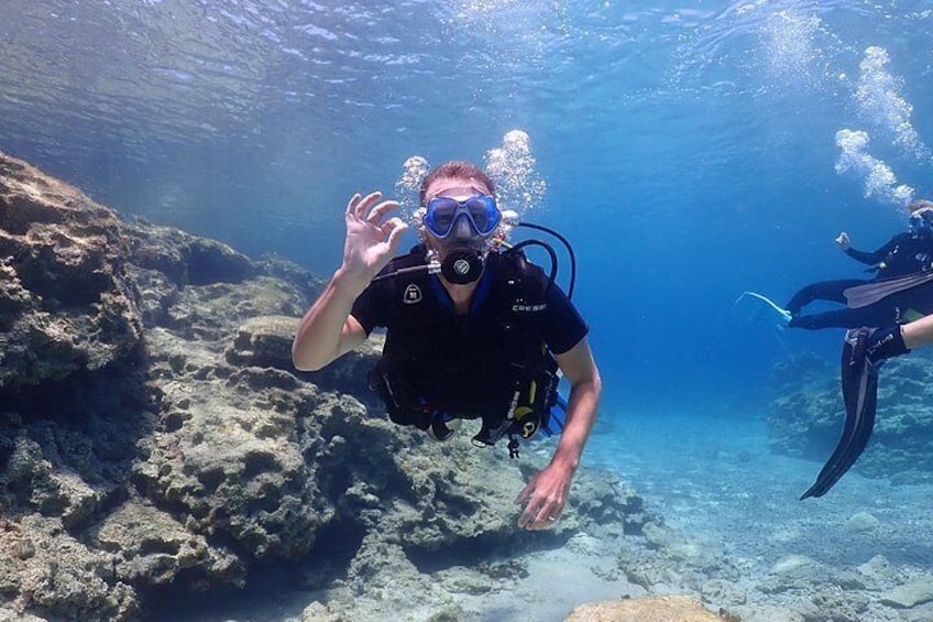 A diver underwater with a rocky seabed and another diver in the background. 3