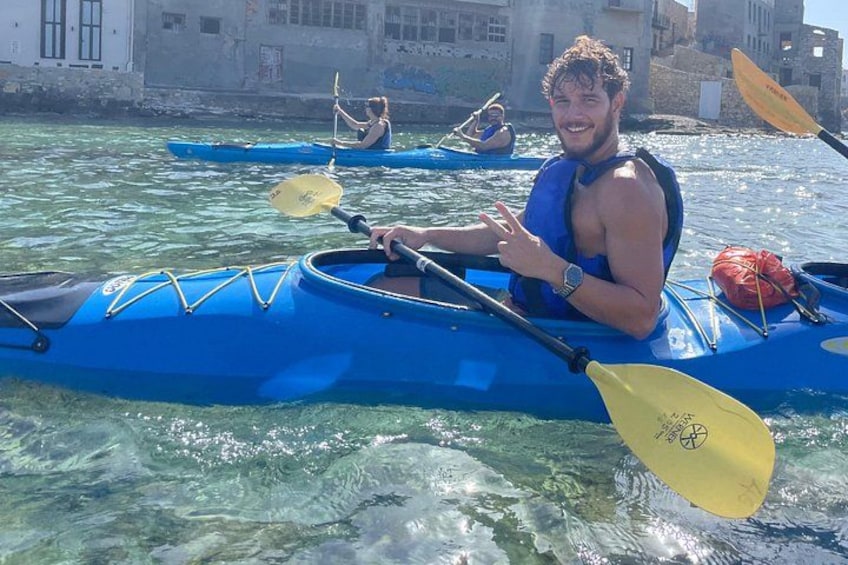 A person kayaking on clear water with buildings in the background. 1
