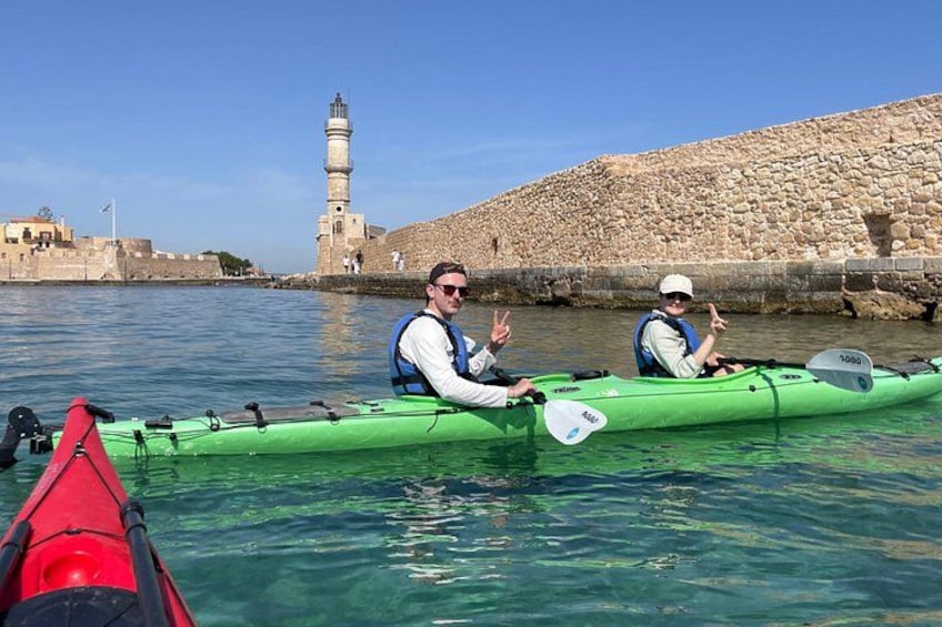 Two people kayaking on a calm body of water with a lighthouse in the background. 3