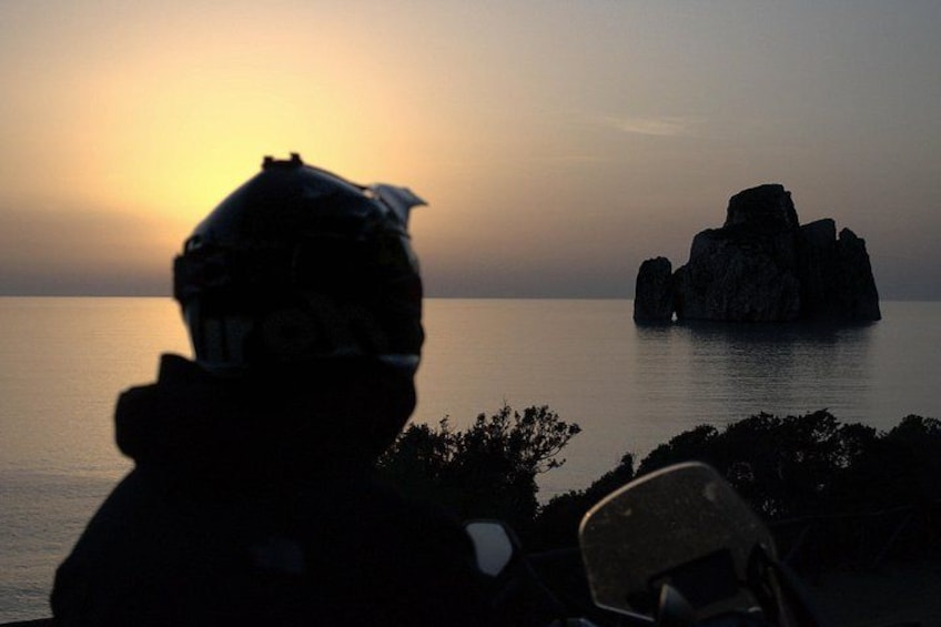 Una persona con una mochila contempla un mar tranquilo con una formación rocosa a lo lejos durante el atardecer. 2