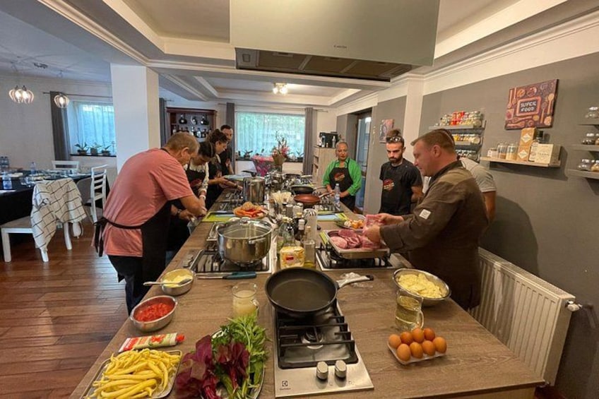 A kitchen with people preparing food, a stove, and various ingredients on the counter. 1