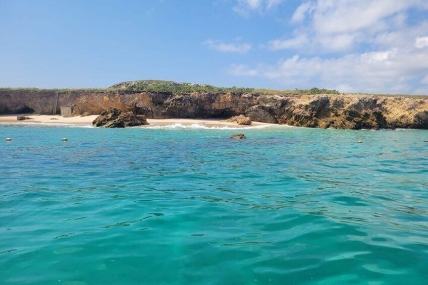 A coastal landscape with clear turquoise waters, sandy beach, and rocky cliffs. 3