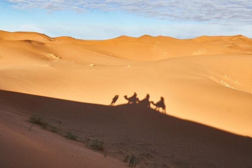 Un paysage désertique avec des dunes de sable et un groupe de personnes chevauchant des chameaux. 3