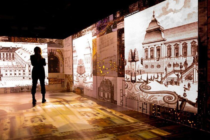 A person standing in a room with large illuminated murals of buildings and architectural designs. 4