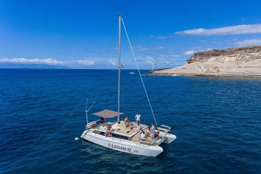 Un voilier nommé « KAUMANT » navigue sur des eaux bleues et calmes, avec une côte rocheuse en arrière-plan. 1