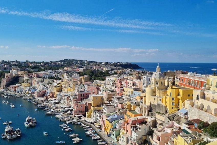 A coastal cityscape with colorful buildings, a harbor filled with boats, and a clear blue sky. 3