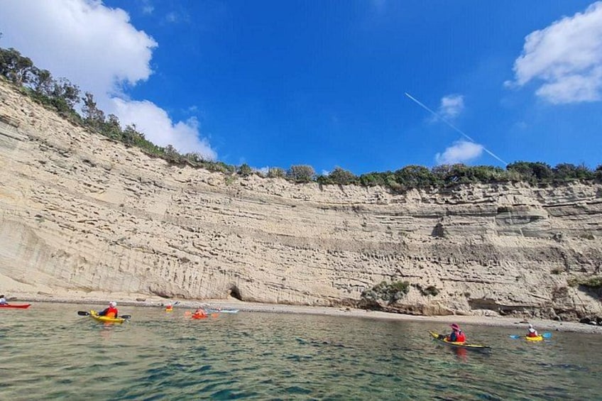 A coastal landscape with kayakers on the water, cliffs, and sparse vegetation. 3