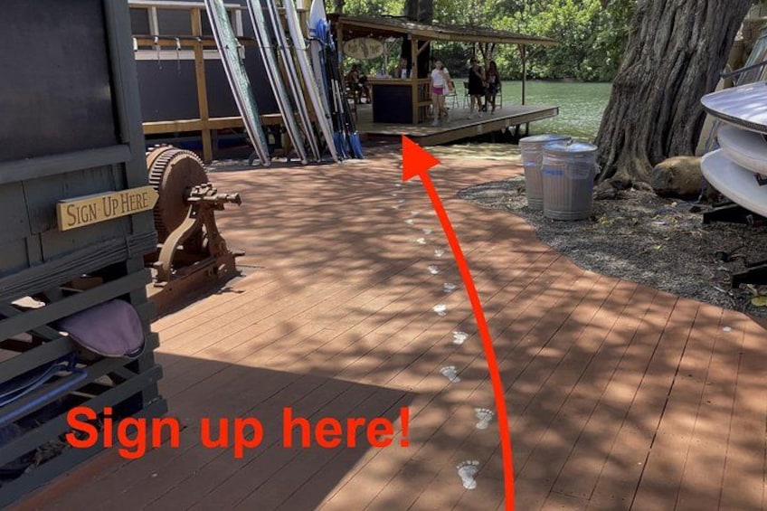 A wooden deck with a sign that reads 'Sign Up Here!' and a red arrow pointing towards a sign-up area. 2