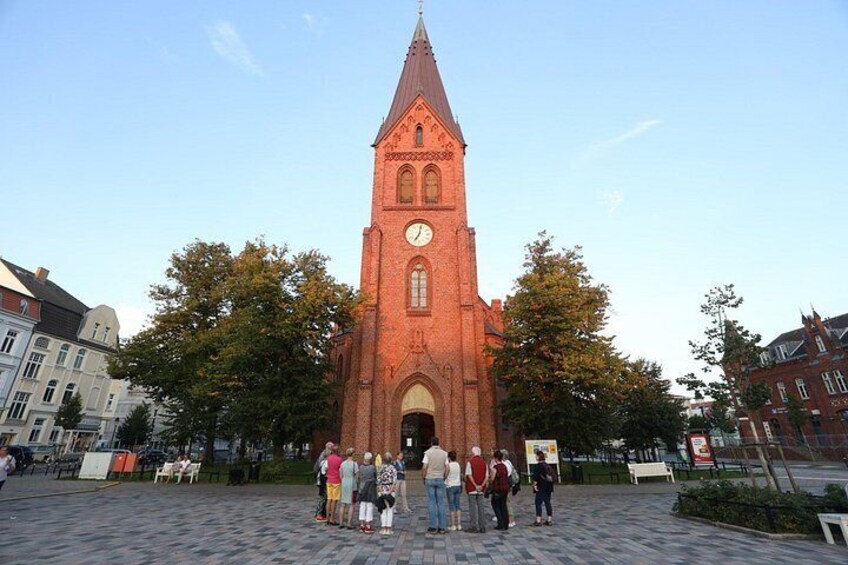 A red brick church with a clock tower, surrounded by trees and people. 5