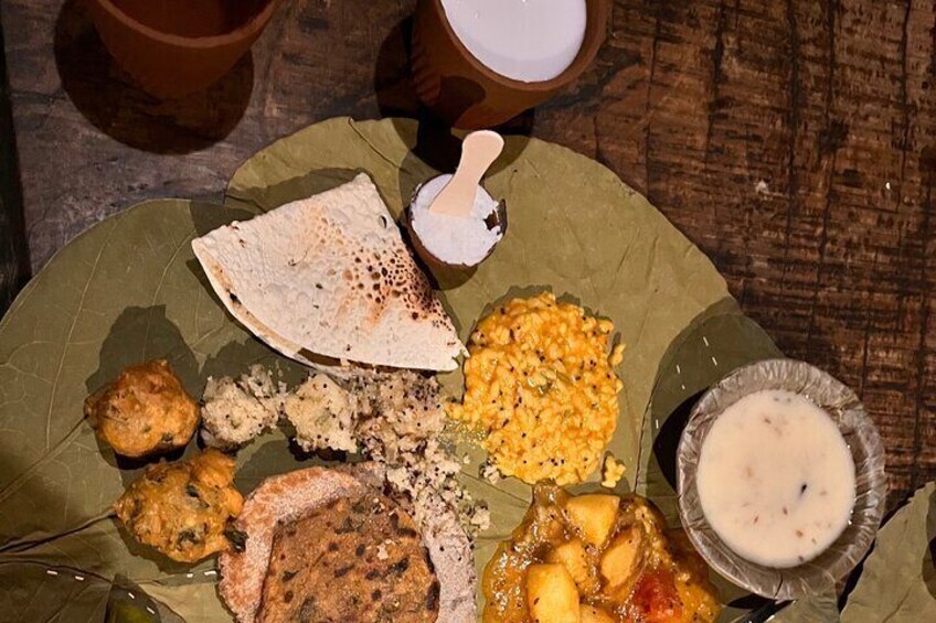 A traditional meal served on a banana leaf with various dishes including a flatbread, a bowl of dal, a piece of fried food, and a small bowl of yogurt. 3
