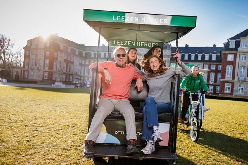 Un grupo de personas en un carrito de golf identificado como 'LEEZEN HEROES' en un parque con edificios al fondo. 3