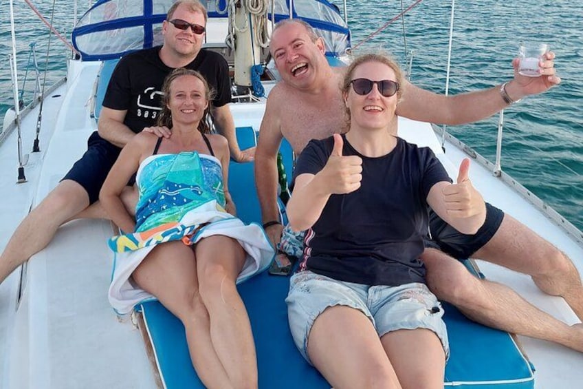 A group of people on a boat with a blue cushion, a man giving a thumbs up, and a woman in a colorful dress. 2