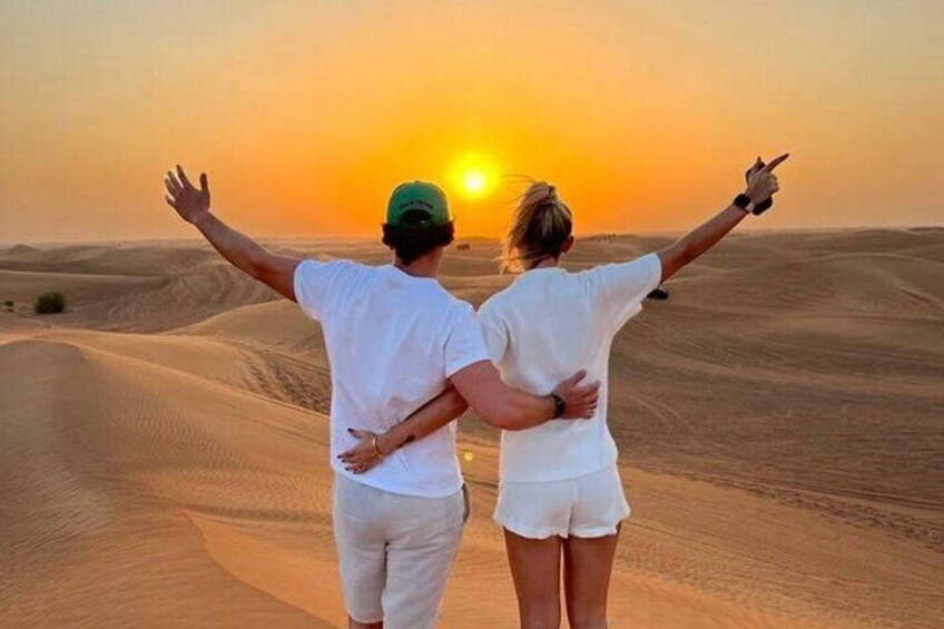 Two people standing in a desert with their arms outstretched towards the sunset. 1