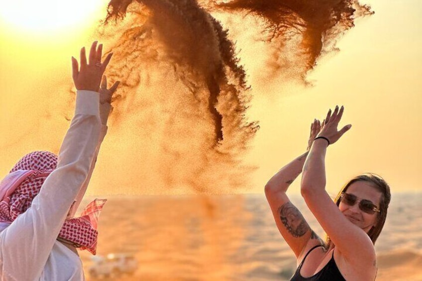 Two people with raised hands, one wearing a checkered scarf, and a large dust cloud in the background. 3