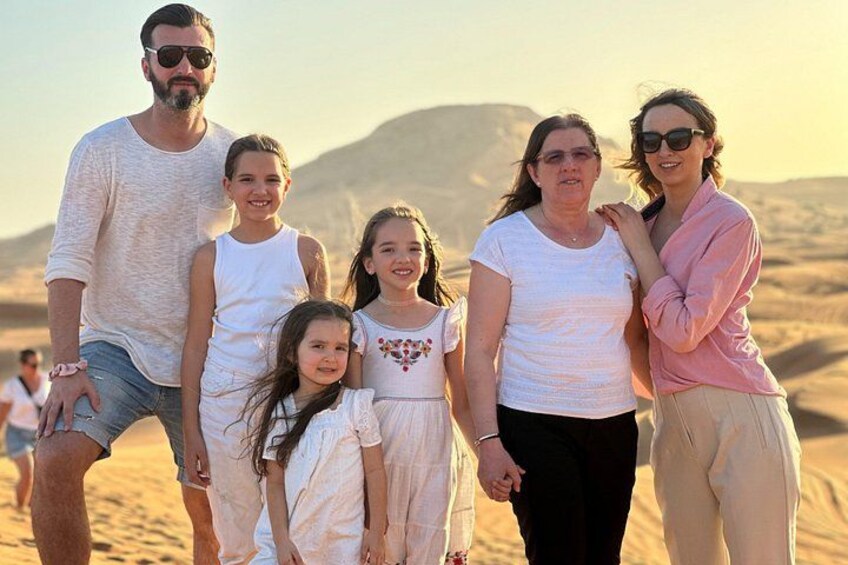 A family of five standing on a sandy beach with a desert landscape in the background. 4