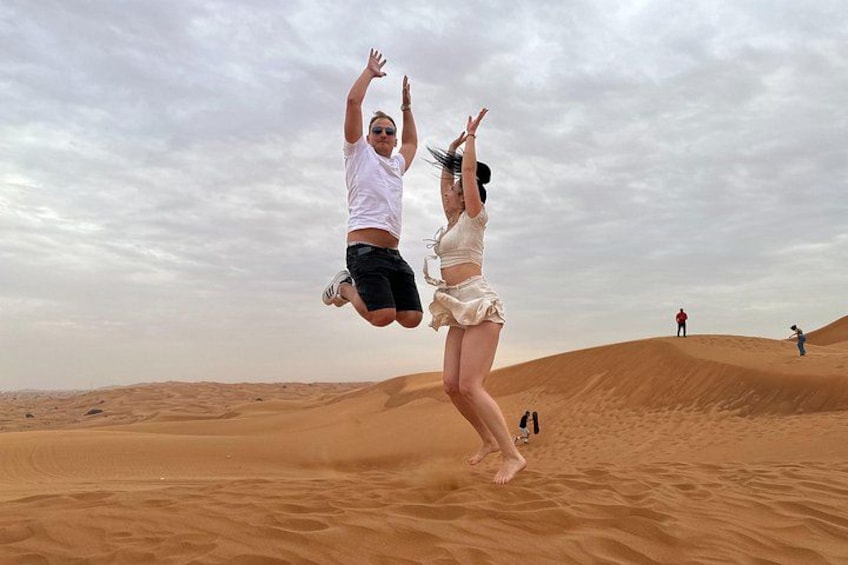 Two people jumping in the air in a desert with sand dunes in the background. 3