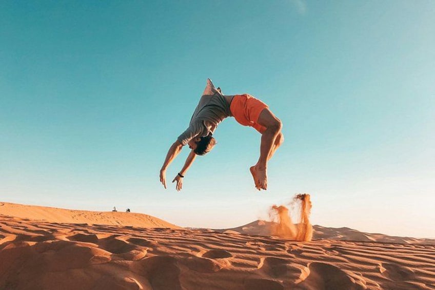 A person performing a flip in the air over a sandy desert landscape. 5