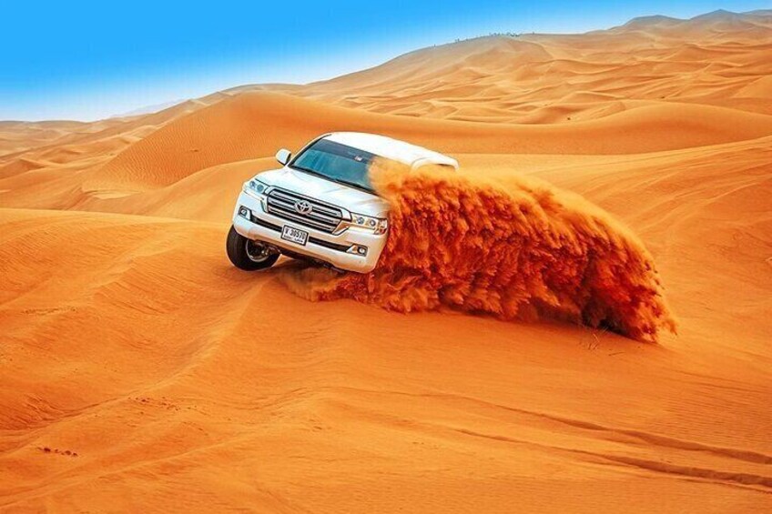 A white SUV driving through a desert with sand being kicked up by its tires. 1