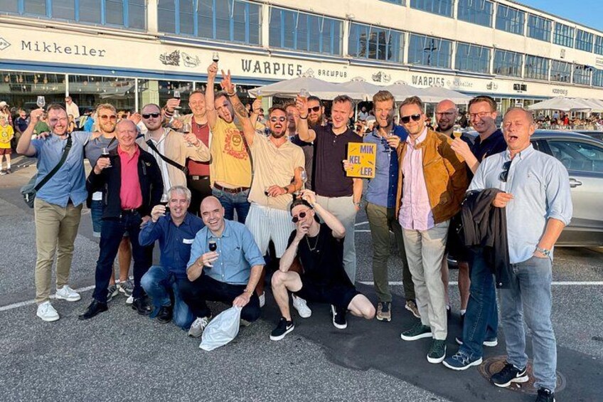 Un gruppo di persone che posa davanti a un edificio con insegne che riportano 'Mikkeller' e 'WARPIGS BREWPUB'. 3