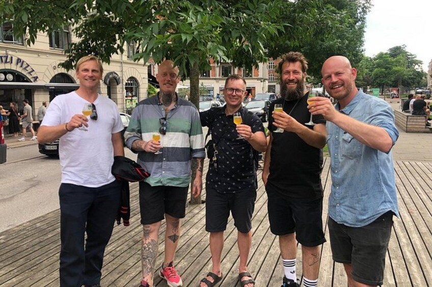 En gruppe mennesker står på en træpromenade, med drikkevarer i hånden. 3