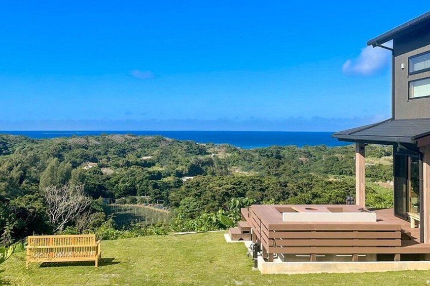 A modern house with a view of the ocean, a grassy lawn, and a wooden bench. 1
