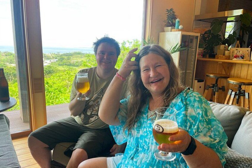 Two people sitting on a deck with drinks, overlooking a lush landscape. 2