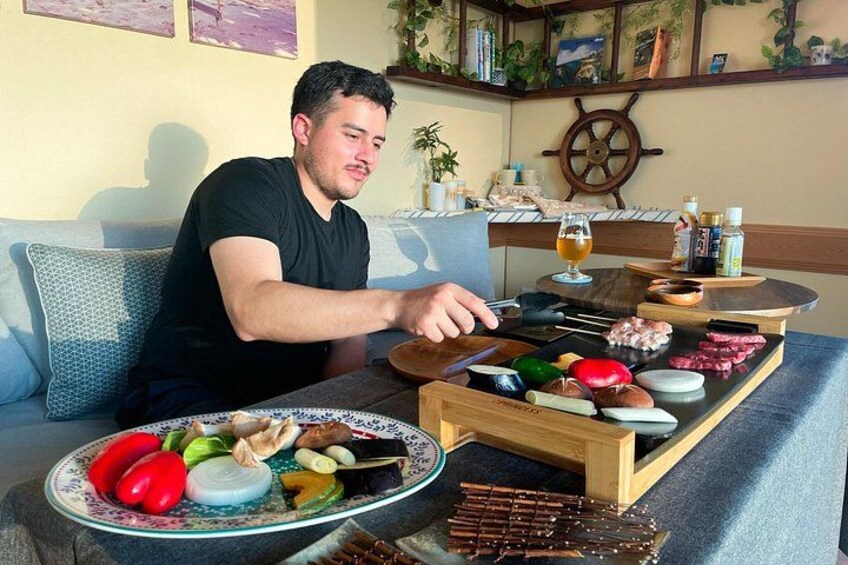 A person grilling various meats and vegetables on a portable grill outdoors. 3