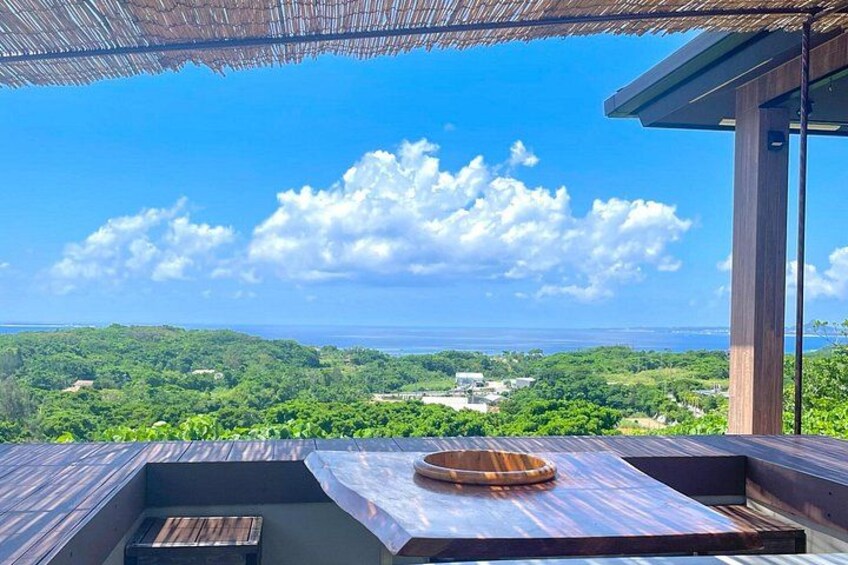 A wooden deck with a table and a bowl, overlooking a lush green landscape and the ocean. 5