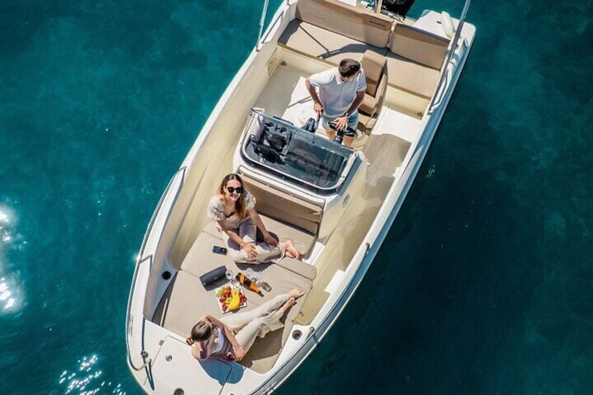 A small boat with three people on board, one standing and two sitting, surrounded by clear blue water. 1