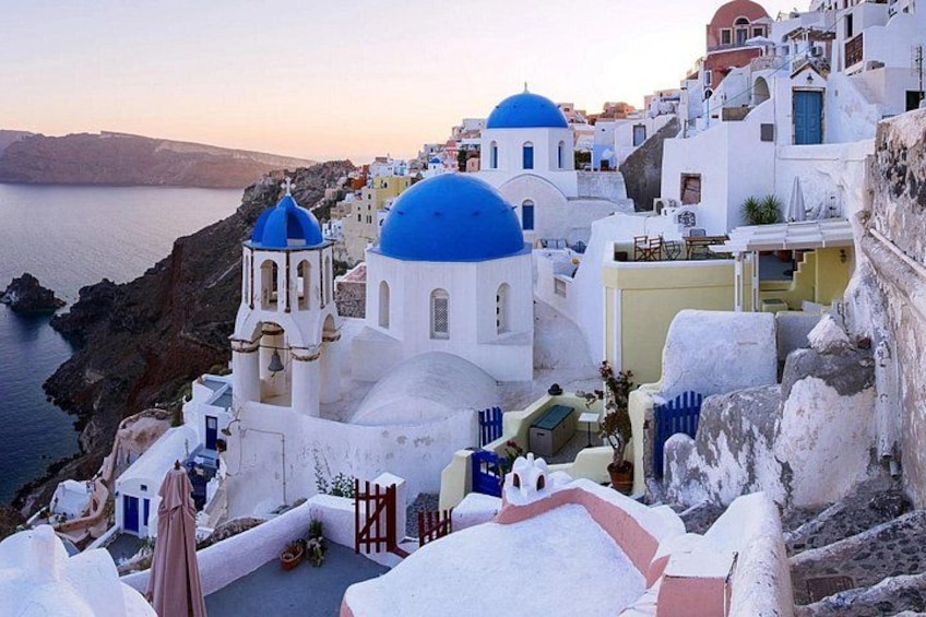 A coastal village with white buildings and blue domes, a rocky coastline, and a clear sky. 3