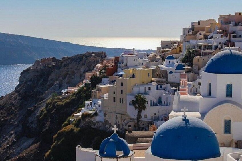 A coastal village with white and blue buildings, a rocky cliff, and the sea in the background. 2