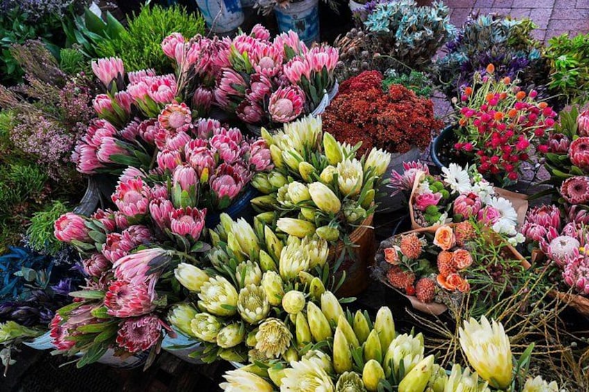 A variety of flowers and plants, including pink, yellow, and red blooms, displayed in pots at a market. 2