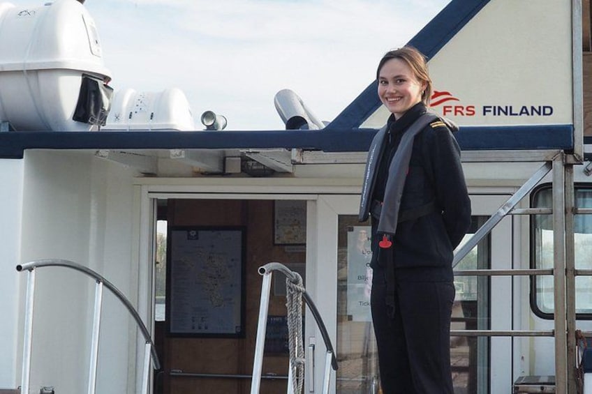 A person in a uniform standing on a ship's deck with a sign reading 'FRS FINLAND' in the background. 2