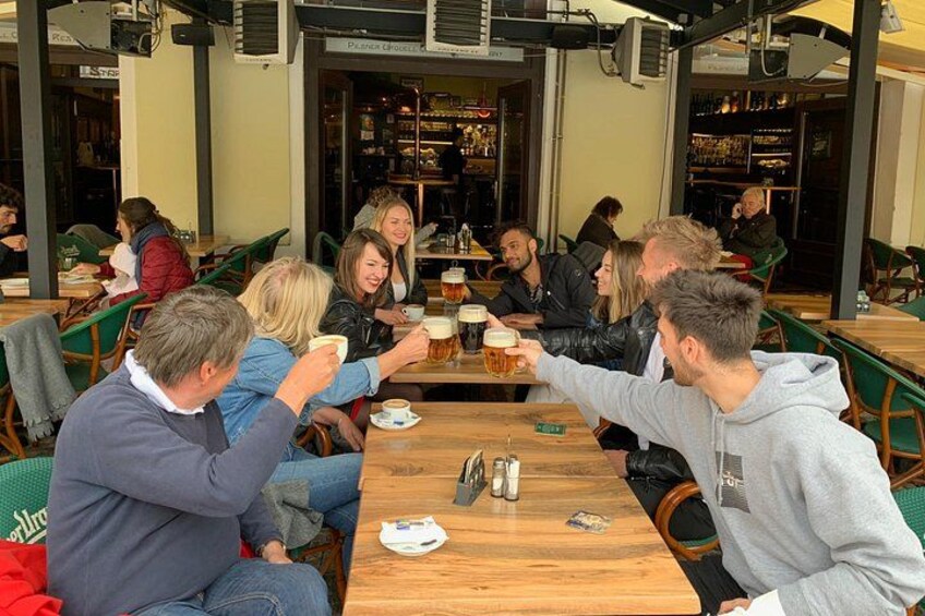 Människor sitter vid bord, dricker öl och umgås på ett café utomhus. 2