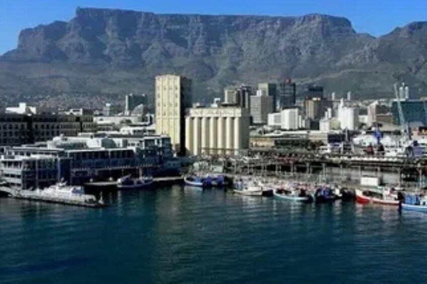 A harbor with boats, a cityscape, and mountains in the background. 1