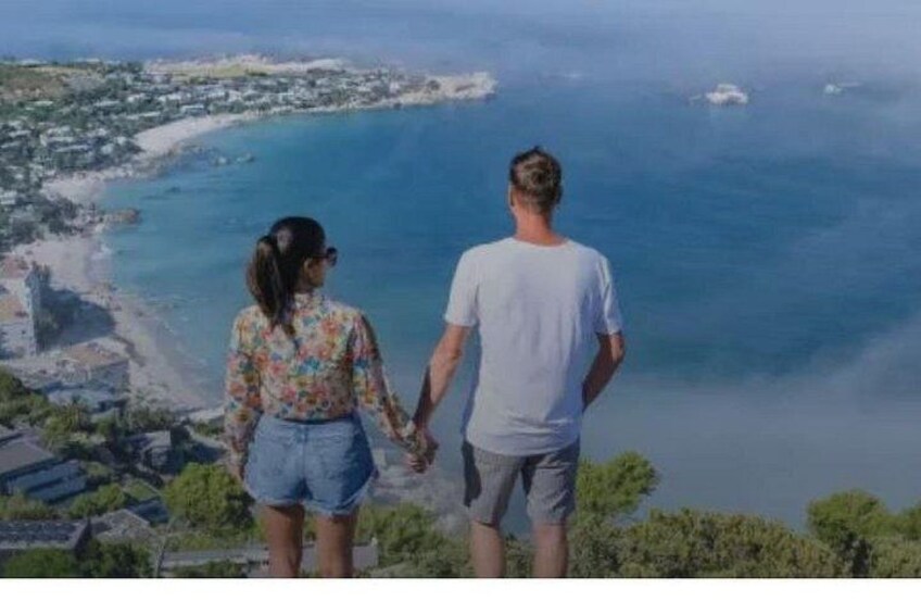 A couple holding hands overlooking a coastal landscape with buildings and a beach. 3