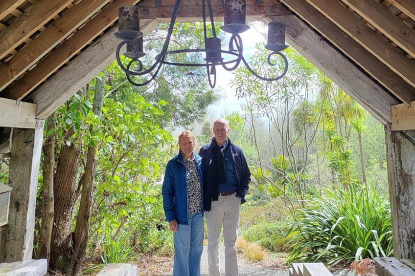 Deux personnes se tiennent sous une structure en bois, avec un luminaire suspendu au-dessus d’elles, le tout étant entouré d’une végétation luxuriante. 4