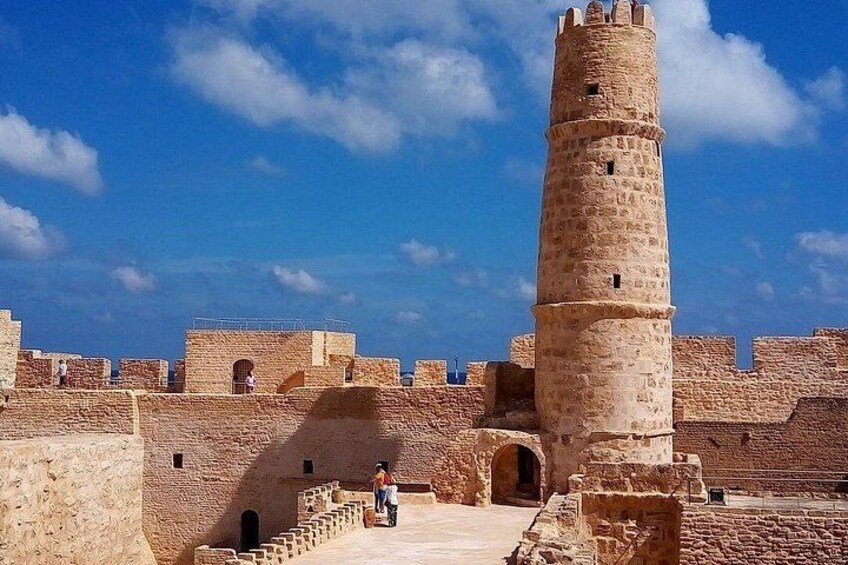 Une forteresse historique en pierre, dotée d’une tour imposante, de portails en arc de cercle et surplombant un ciel d’un bleu éclatant. 4